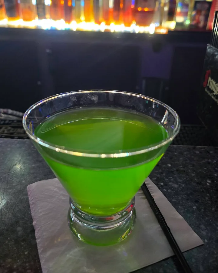 A bright green martini on the bar top at Sugar Bar, backlit bottles out of focus behind it